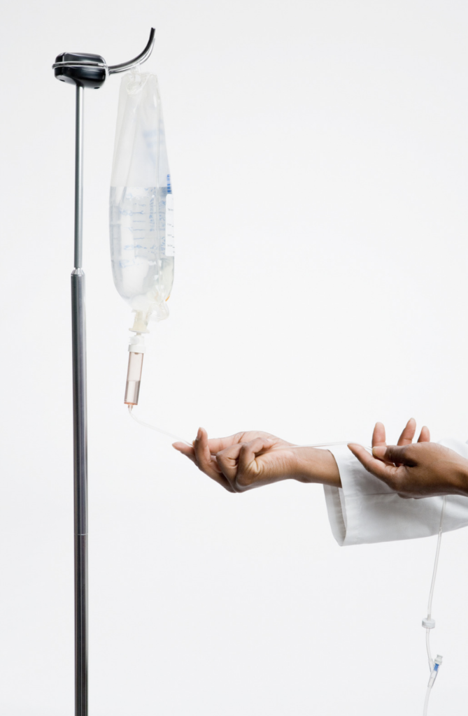 A person adjusting an intravenous (IV) line with a fluid bag on a stand.